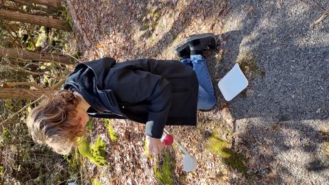 Connor kneeling down on leafy ground, near edge of watery area in forest, holding insect collecting tools