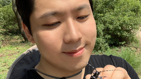 Sangil Kim holding an Anoplophora outdoors, trees in background
