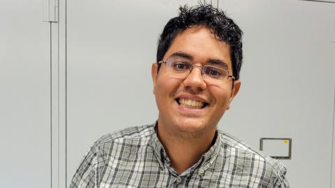 Thalles Lavinscky Pereira, smiling and holding a drawer of insect specimens, in front of gray collections cabinets