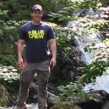 Patrick Gorring standing in rocky, wooded location near a stream