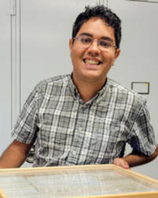 Thalles Lavinscky Pereira, smiling and holding a drawer of insect specimens, in front of gray collections cabinets