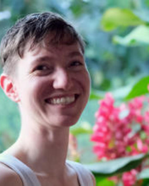Portrait of Valentine Bouju, smiling, with short hair, blurred foliage background