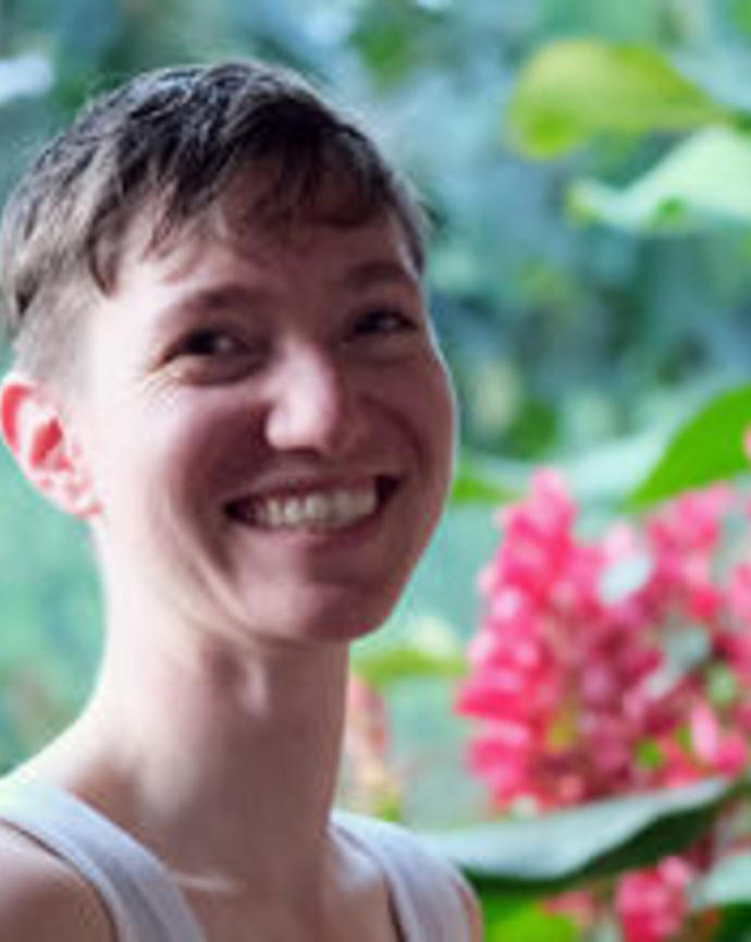 Portrait of Valentine Bouju, smiling, with short hair, blurred foliage background